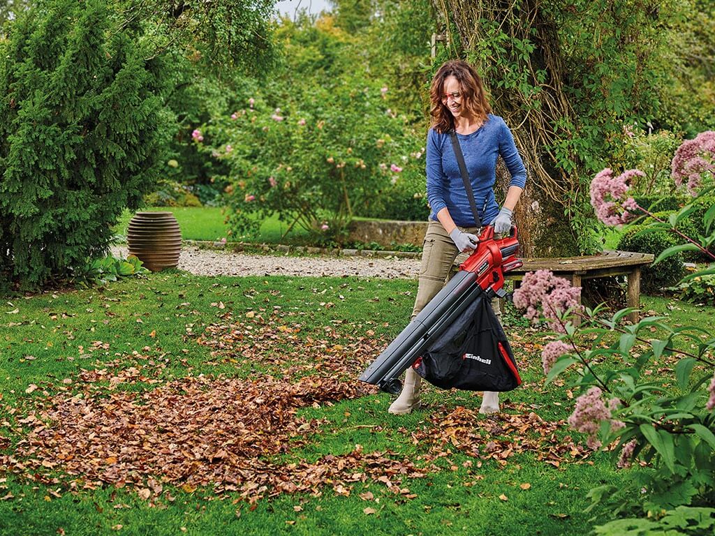 Une femme dans le jardin aspire les feuilles d'automne avec un aspirateur à feuilles sans fil Einhell.