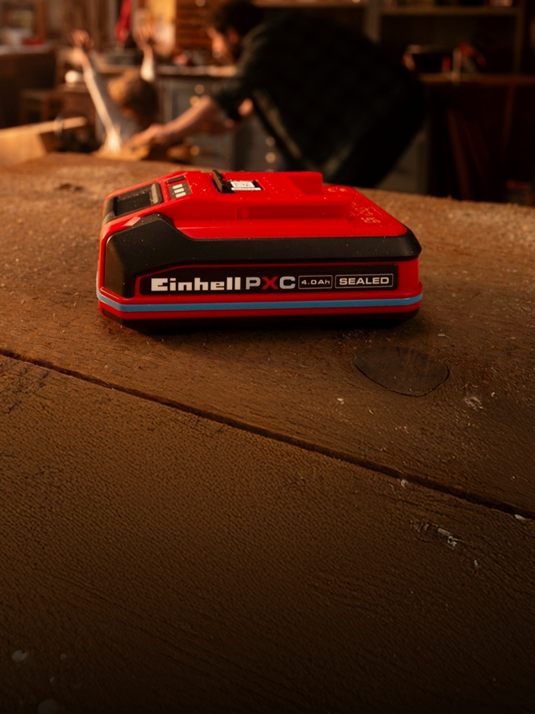 Batterie Einhell Power X-Change SEALED de 4,0 Ah posée sur un établi en bois, avec anneau bleu et marquage visibles.
