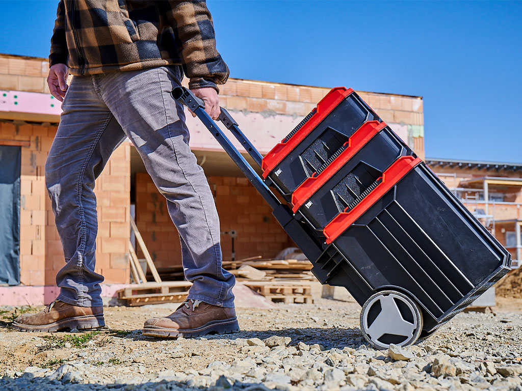 A man dragging the Einhell E-Case Tower over stony ground.