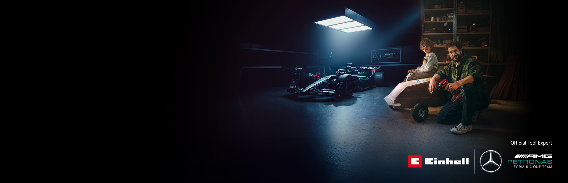 Un père et son enfant dans un atelier avec une voiture à savon faite maison. À l’arrière-plan, une voiture de Formule 1 Mercedes-AMG PETRONAS et des outils Einhell.