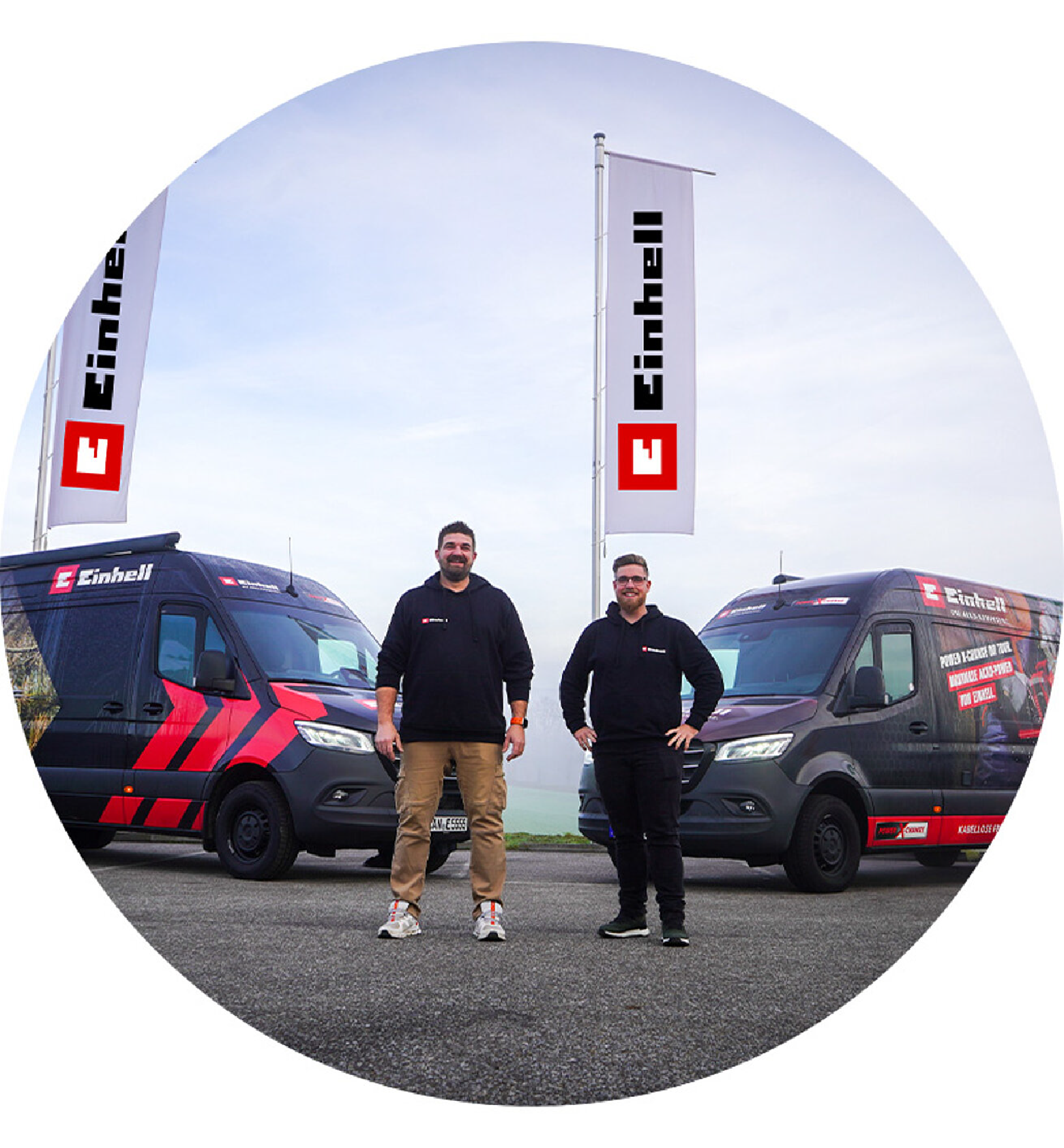 Two Einhell team members standing between branded Einhell vans with Einhell flags in the background